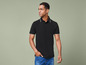 Man draagt een zwart polo shirt met witte boord en blauwe jeans.
