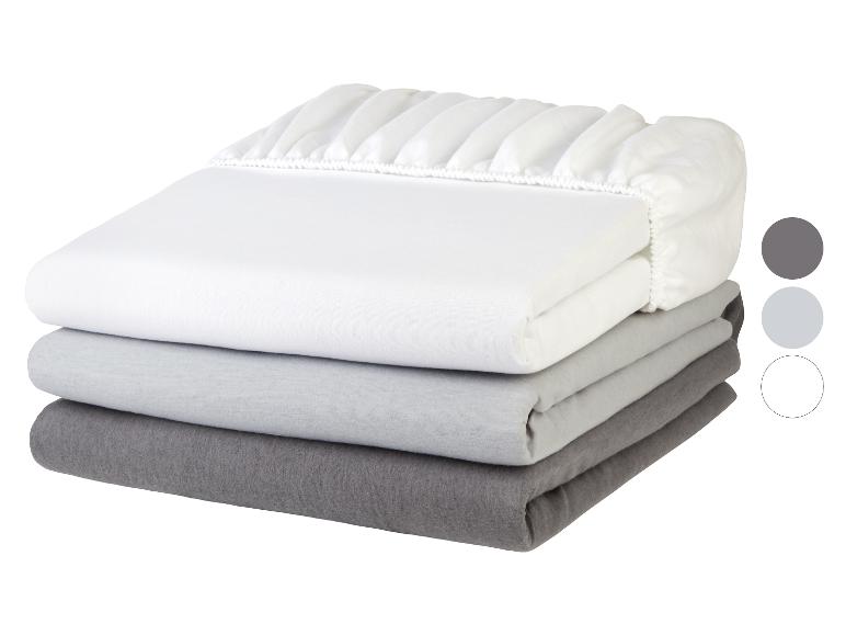 Drie opgevouwen grijze en witte hoeslakens in een stapel, met elastische randen.