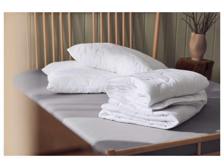 Wit kussen en dekbed op een grijs bed, met een houten achtergrond.