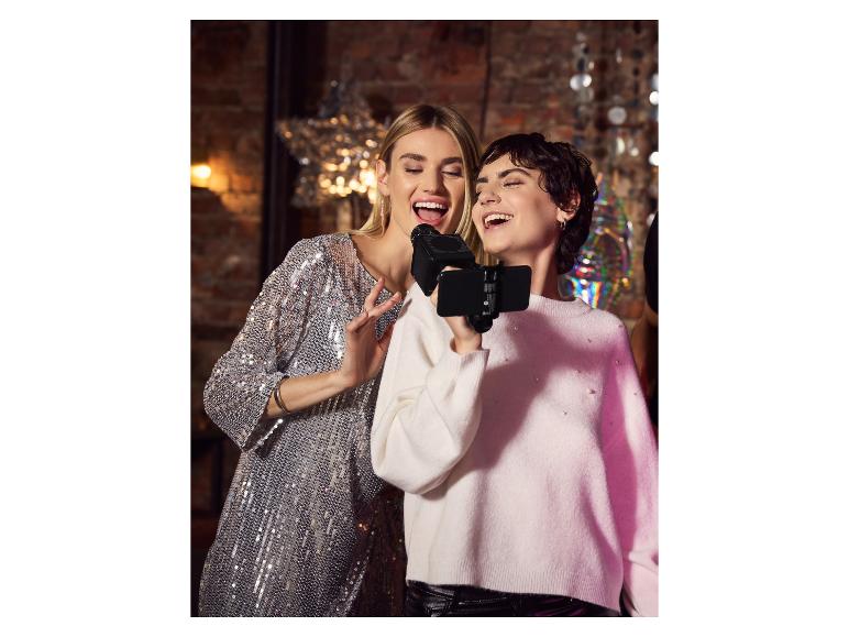 Twee vrouwen zingen karaoke met een microfoon en smartphone op een feestje.