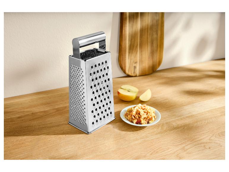 Roestvrijstalen rasp met geraspte appels op een houten aanrecht.