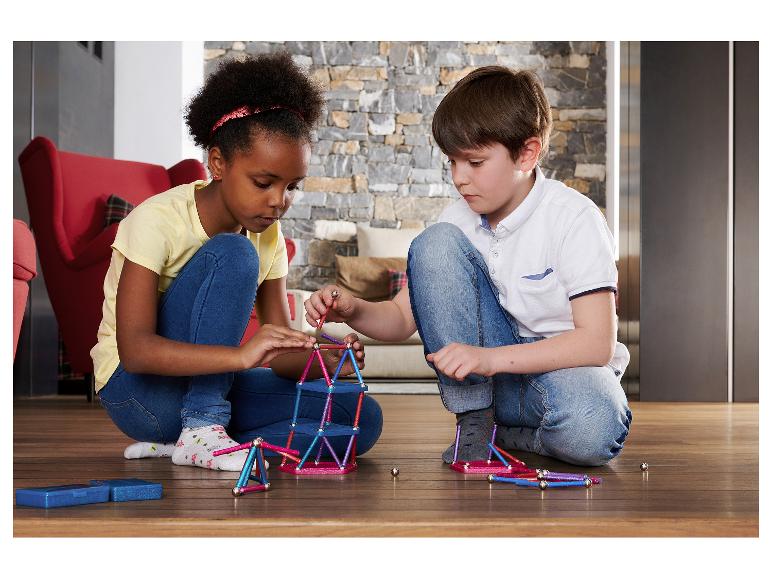 Twee kinderen spelen met magnetisch constructiespeelgoed op een houten vloer.