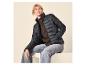 Vrouw in zwart gewatteerd jack en jeans, zittend en glimlachend.