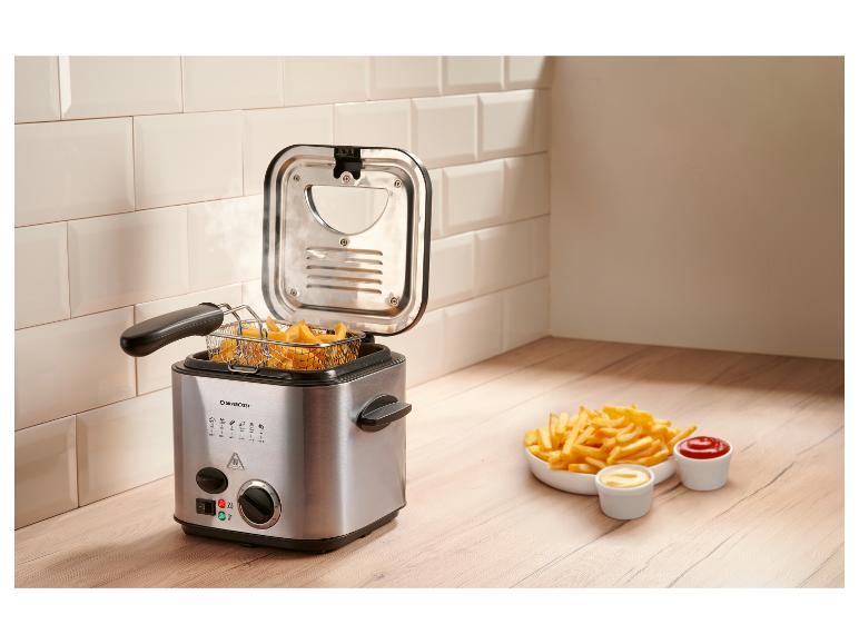 Friteuse met friet en sauzen op een houten aanrecht.