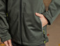 Een groene softshell jas met gele ritsen en een merklogo.