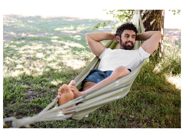 Man in een wit T-shirt en korte broek ontspant in een hangmat buiten.