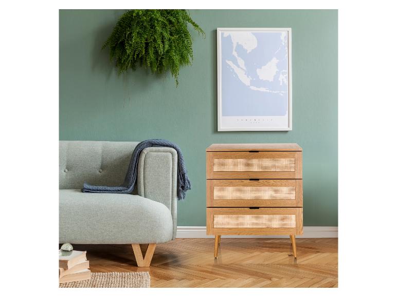 Woonkamer met groene muur, bank, rotan ladekast en ingelijste kaart.