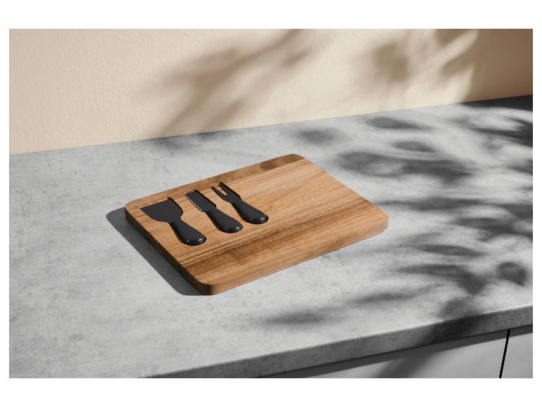 Houten kaasplank met drie zwarte kaasmesjes op een grijs aanrecht.