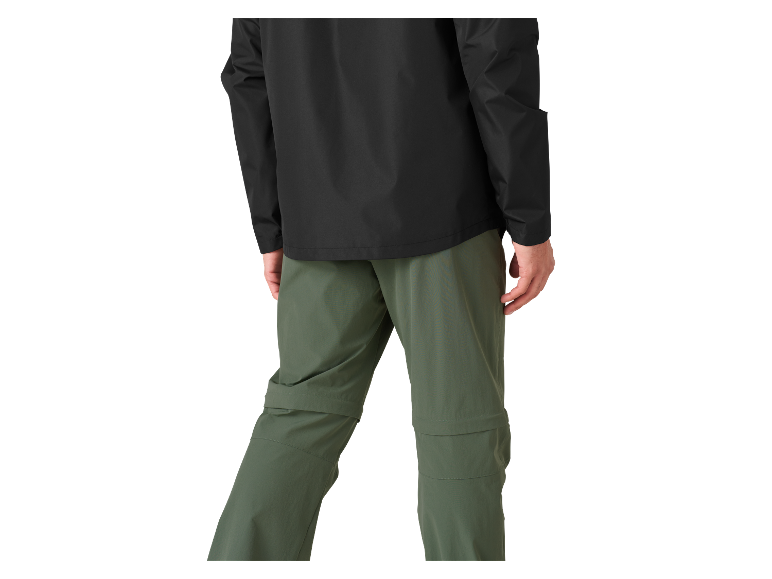 Man in een zwart jack en groene broek met rits.