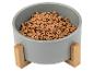 Een grijze hondenvoerbak met houten standaard, gevuld met hondenbrokken.