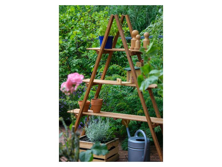Houten rek met planten, potten en tuindecoraties in een weelderige tuin.