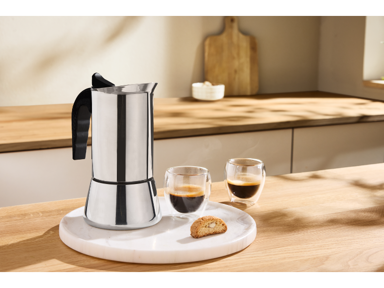 Roestvrijstalen espressopot met twee espressokopjes en een biscotti op een marmeren dienblad.