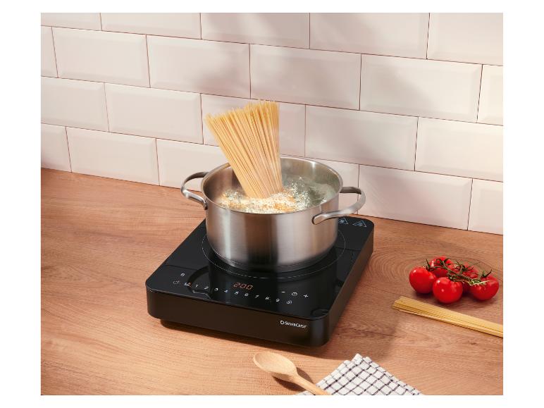 Spaghetti koken in een pan op een inductiekookplaat, tomaten en rauwe spaghetti op het aanrecht.