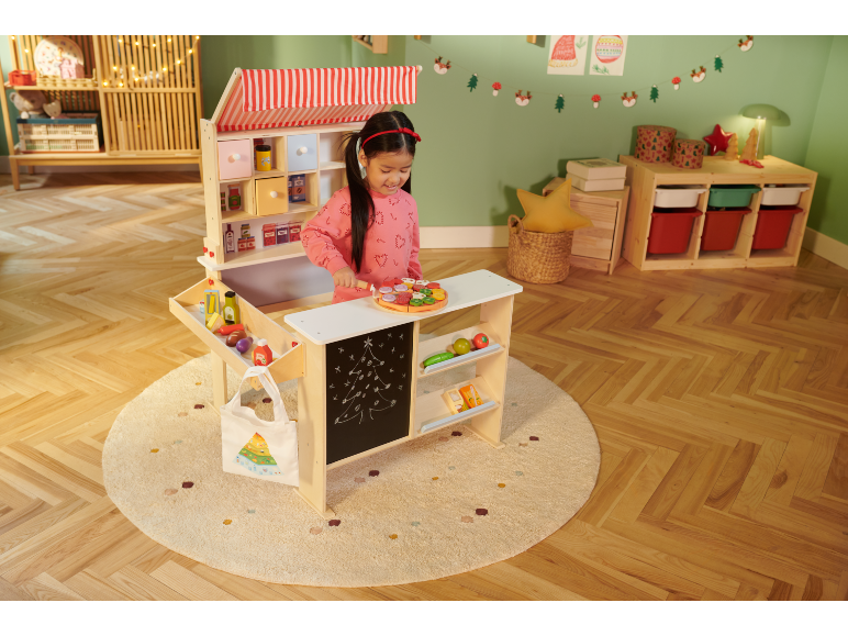 Meisje speelt met een houten speelgoedwinkel, versierd in kerststijl.
