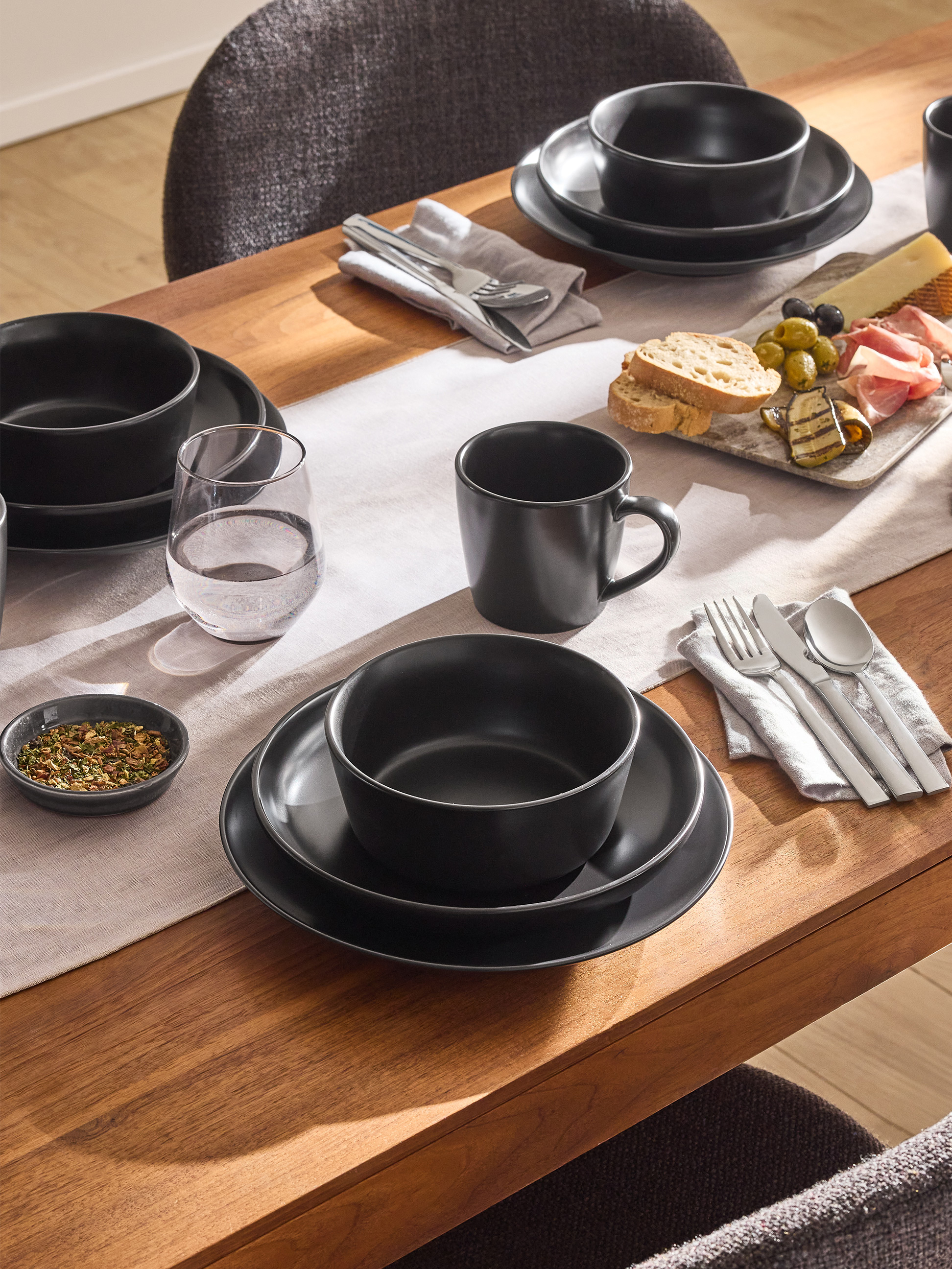 Eettafel gedekt met zwart steengoed servies, bestek en een antipastischotel.