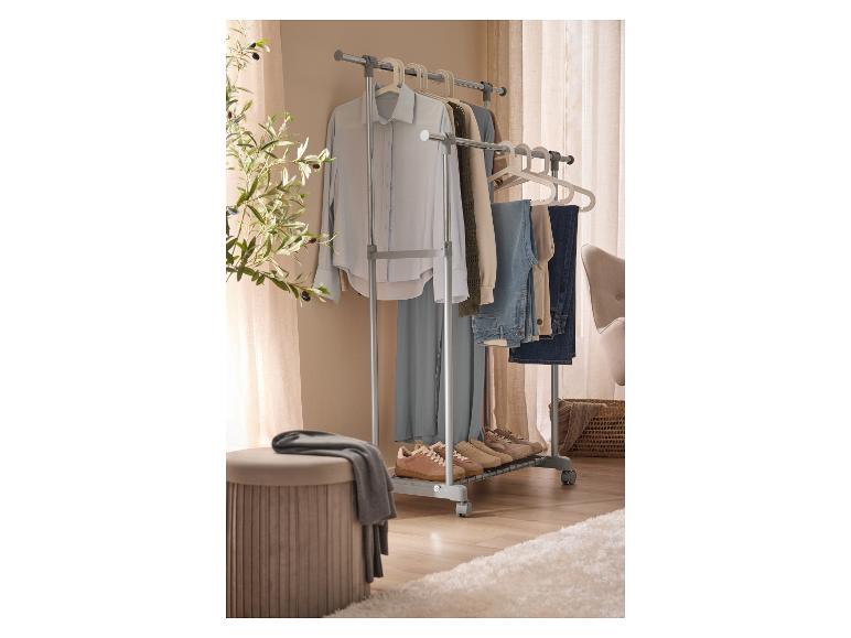 Een mobiel kledingrek met kleding, schoenen en een poef in een kamer.