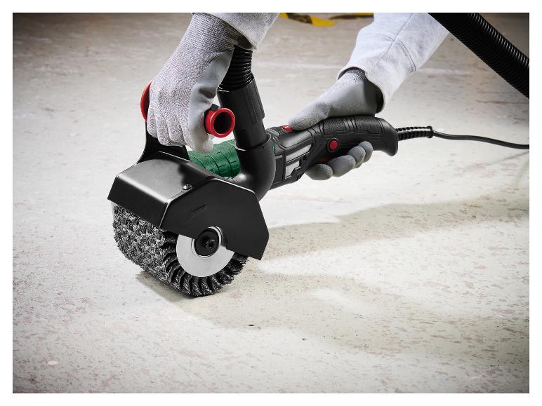 Elektrisch borstelgereedschap met staalborstel, vastgehouden door gehandschoende handen op betonnen vloer.