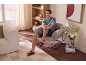 Man in korte broek en sandalen, zittend in een fauteuil in een moderne woonkamer.