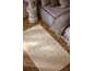 Beige vloerkleed met reliëf rozenpatroon in een slaapkamer met bed en nachtkastje.