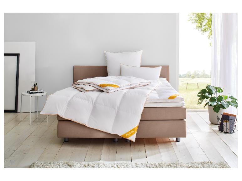 Palette Good Edition dekbed en kussens op een bed in een lichte kamer met raam.