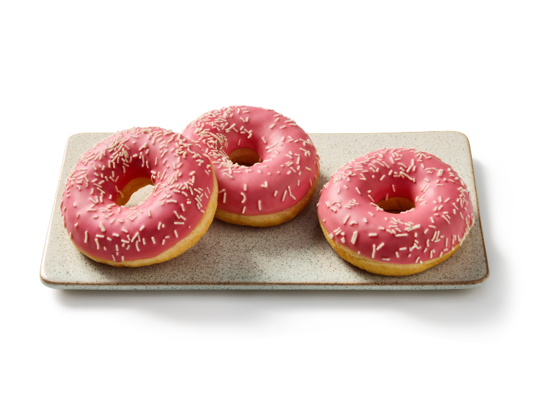 Drie roze geglazuurde donuts met sprinkles op een rechthoekig bord.