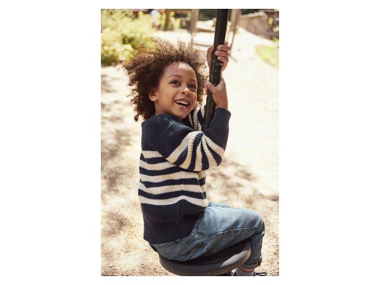 Een blije jongen in een gestreepte trui en spijkerbroek op een schommel.