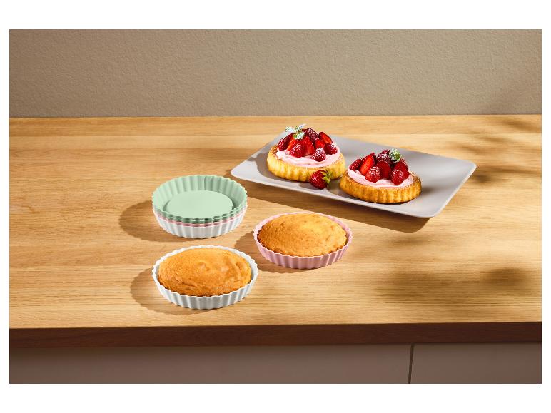 Aardbeientaartjes en gebak in siliconen vormen op een houten tafel.