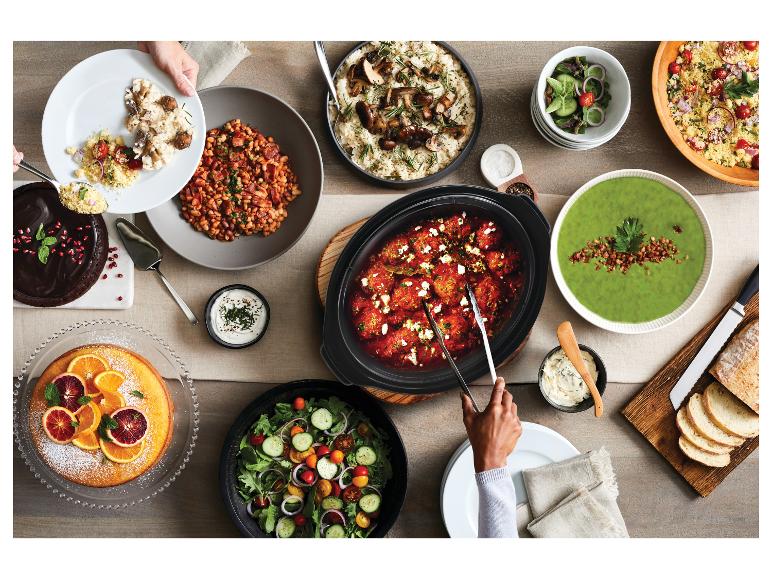 Een tafel gedekt met verschillende gerechten, waaronder gehaktballetjes in tomatensaus, groene soep en salade.
