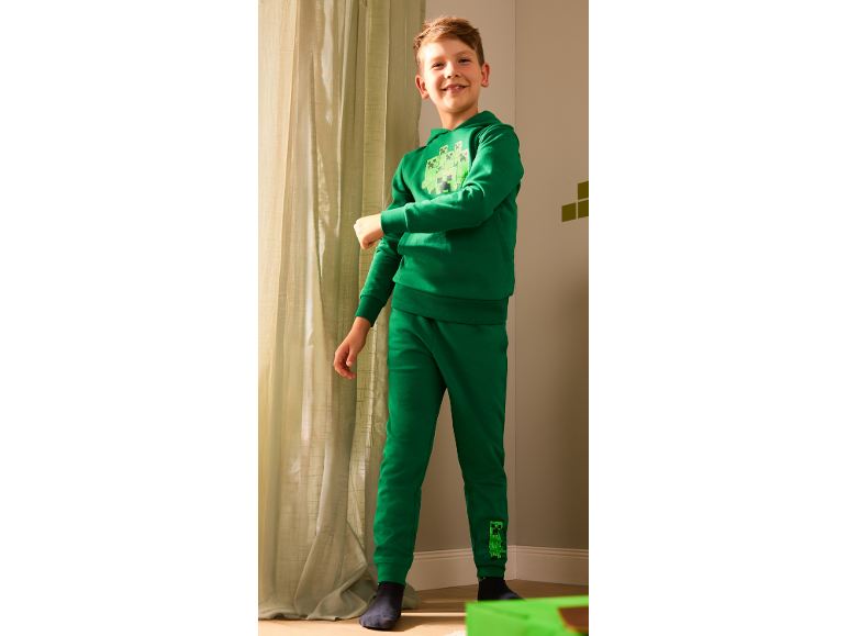 Lachende jongen in groene hoodie en joggingbroek met monsterprint.