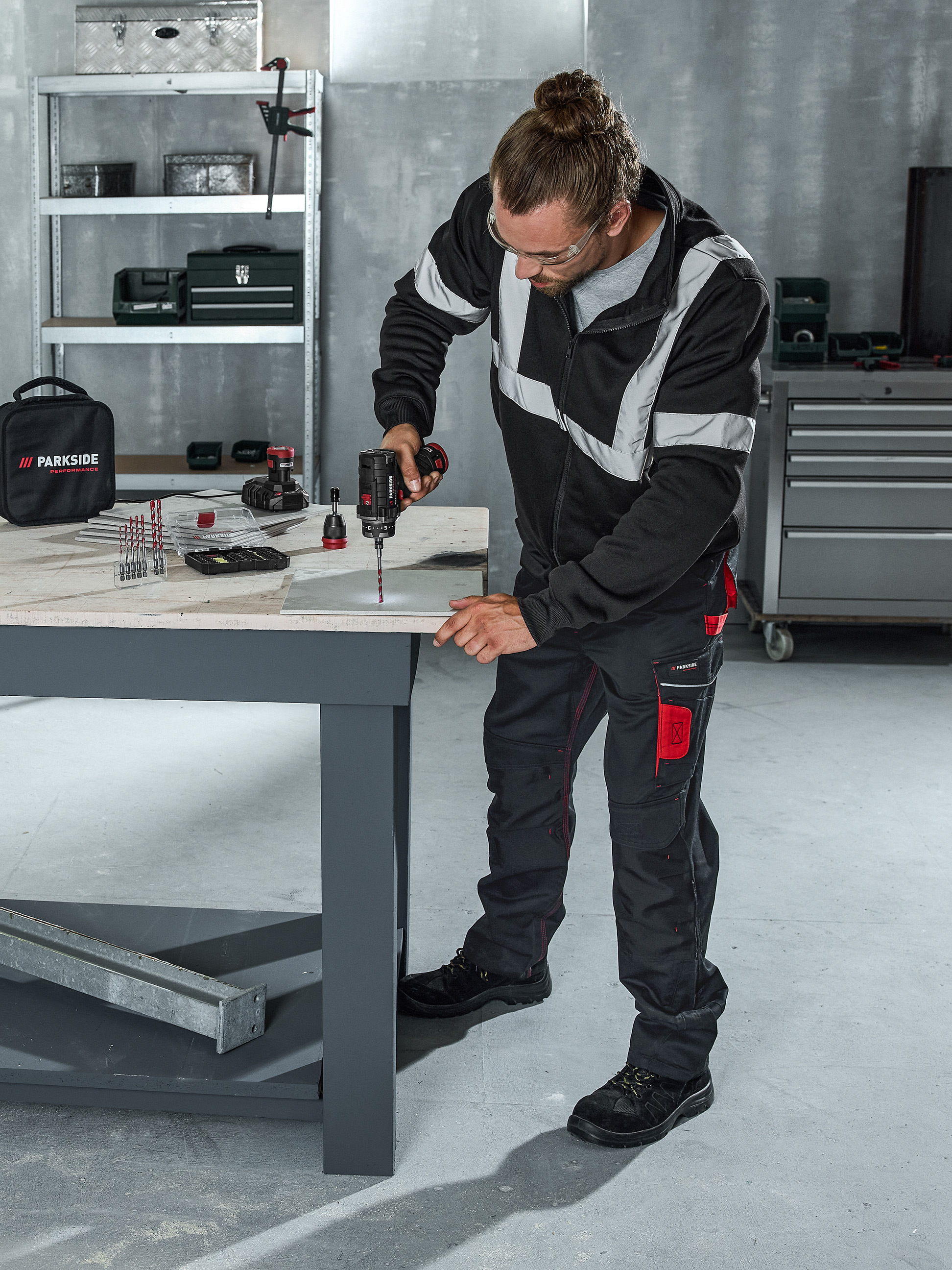 Man boort in een oppervlak met een accuboormachine, omringd door diverse boren en gereedschap.