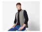 Een man draagt een grijze gewatteerde vest en een donkerblauwe jeans.
