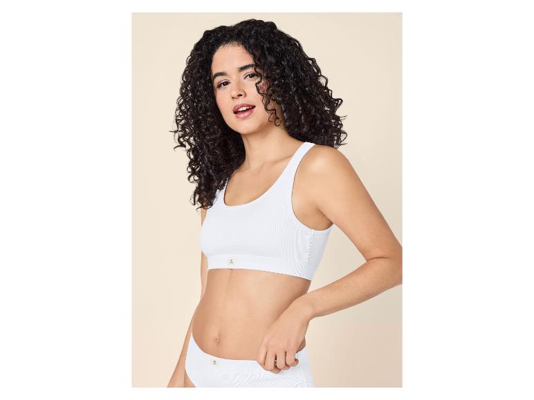Vrouw met krullend haar draagt een witte geribbelde bralette en bijpassende slip.