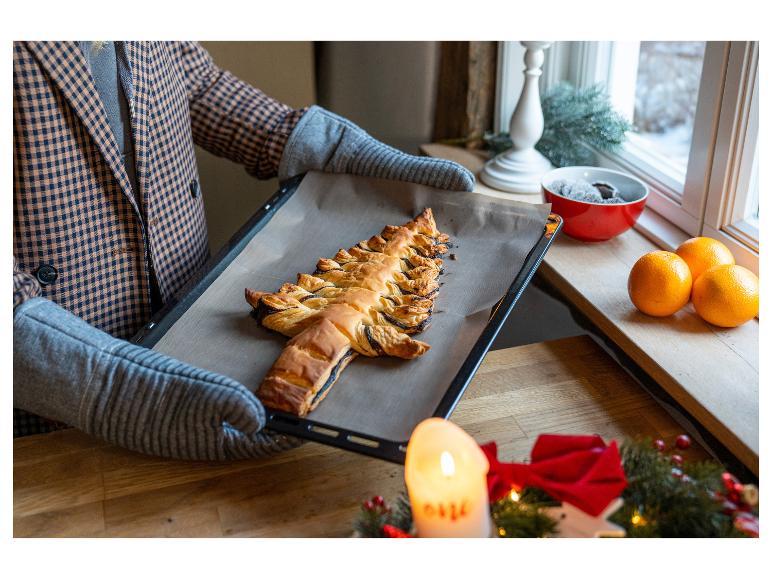 Iemand houdt een bakplaat vast met een kerstboomvormige taart.