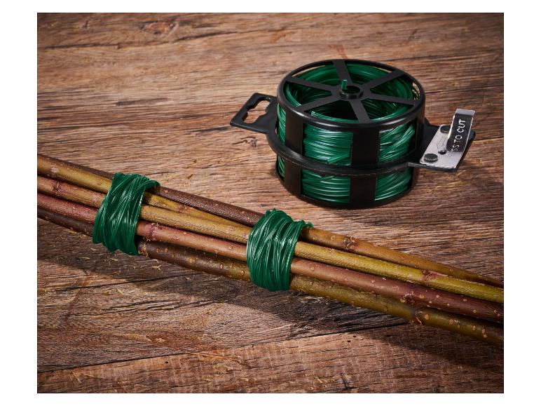 Groene tuindraad in dispenser met snijder en een bundel takken gebonden op een houten achtergrond.