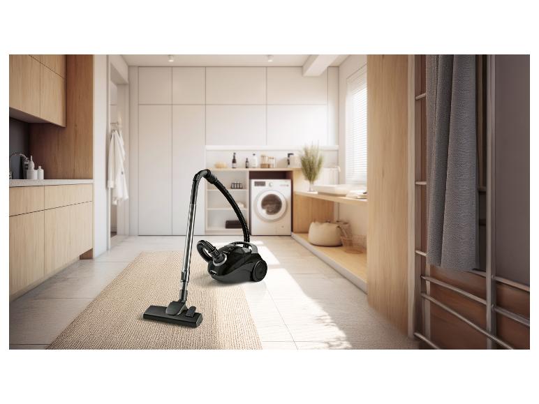 Zwarte stofzuiger op een vloerkleed in een moderne wasruimte met wasmachine.