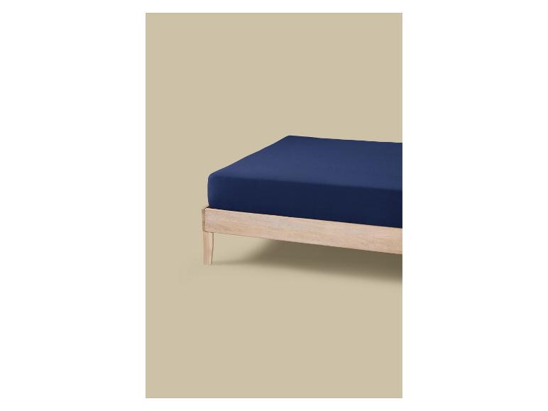 Een bed met een licht houten frame en een matras bedekt met een donkerblauw hoeslaken.