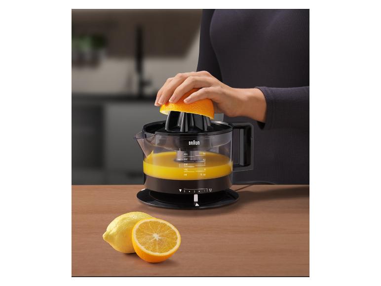 Vrouw perst een sinaasappel met een citruspers, met citroenen en sinaasappels op een houten tafel.