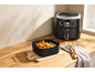 Zwarte siliconen vorm voor heteluchtfriteuse met eten op een houten plank.