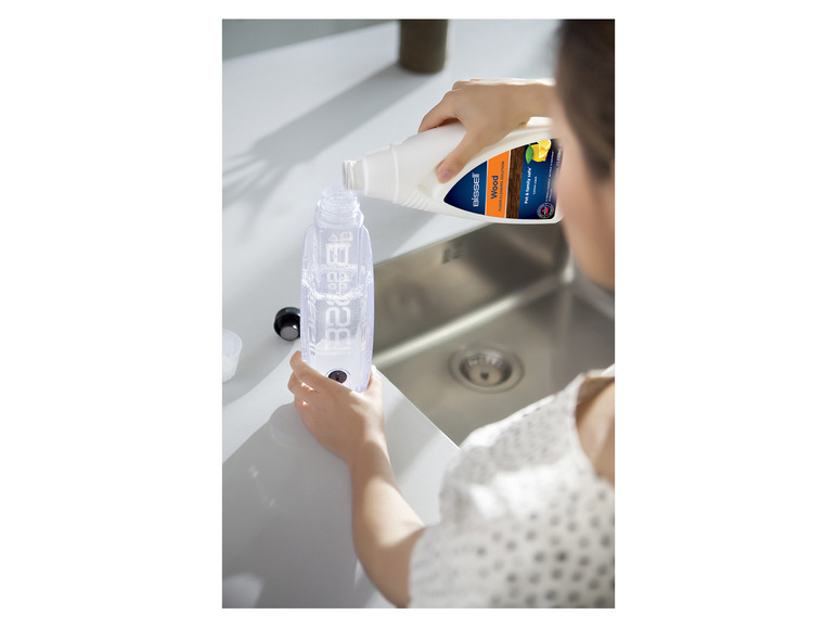 Een vrouw giet Bissell Wood vloerreiniger in een fles.