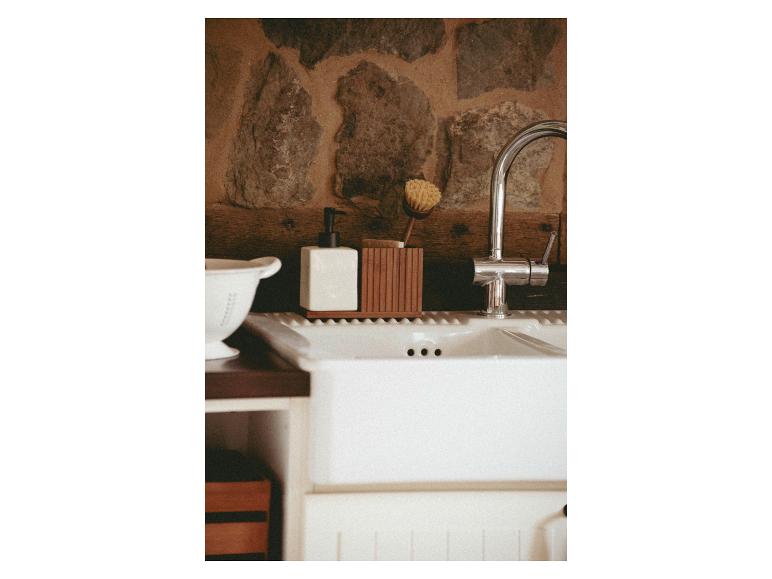 Een witte keramische zeepdispenser en een houten borstelhouder staan op een keuken gootsteen.
