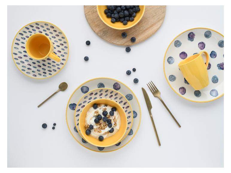 Ontbijtsetting met gele kommen en borden, yoghurt met bosbessen en granola, en losse bosbessen.