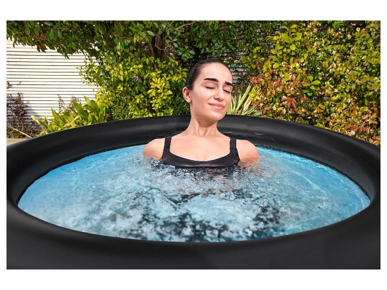 Vrouw ontspant in een buitenjacuzzi, omringd door groen.