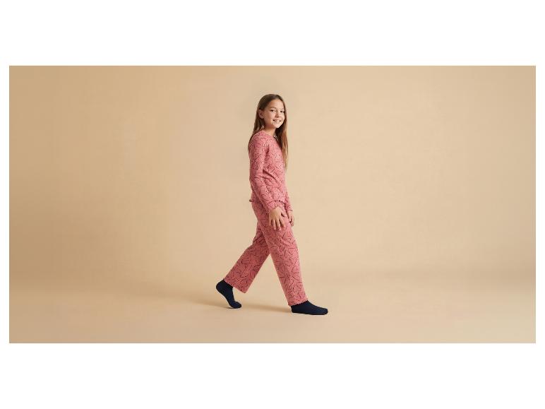Meisje in roze pyjama met zwarte hartenprint en donkerblauwe sokken.