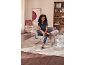 Vrouw zit in fauteuil in moderne woonkamer, draagt poloshirt en gestreepte broek.