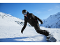 Snowboarder in zwarte jas en broek, met helm en bril, daalt een besneeuwde berghelling af.