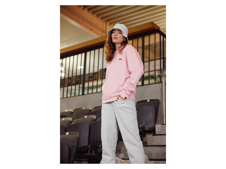 Een vrouw draagt een roze Ellesse hoodie en grijze Ellesse joggingbroek.