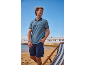 Man in blauwe poloshirt en blauwe cargoshorts op het strand met ligstoel.