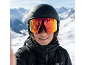Vrouw met zwarte skihelm en skibril met reflecterende glazen in besneeuwde bergen.