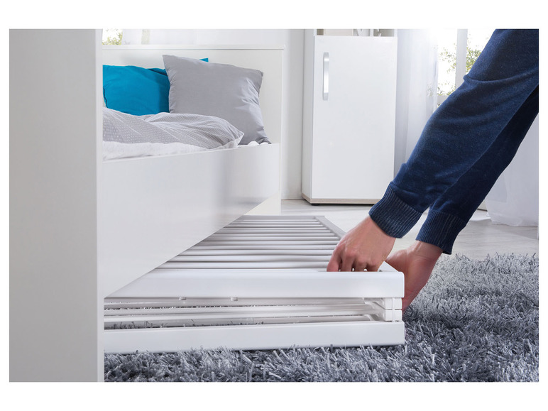 Een persoon trekt een bedlade uit een wit bed.
