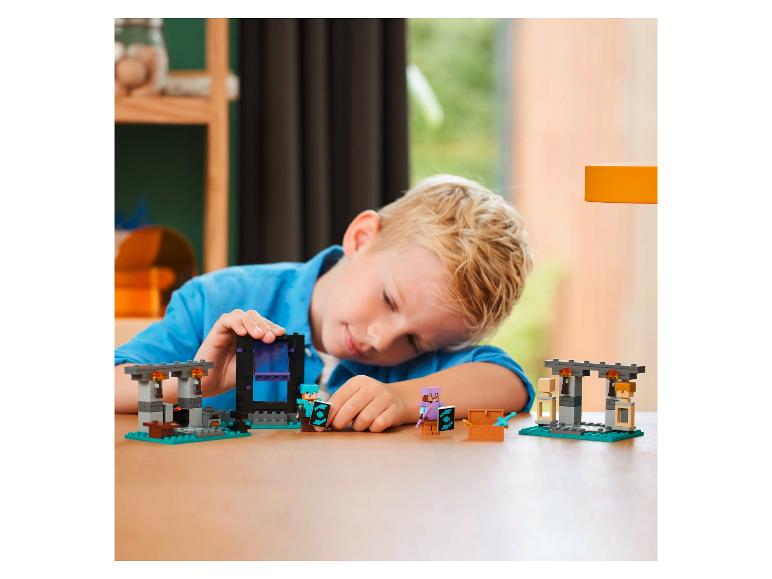 Een kind speelt met een LEGO Minecraft set met een Nether-portaal en figuren.